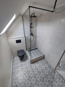 Elkészült tetőtéri fürdőszoba fekete fali WC-vel és üvegfalú zuhanyzóval